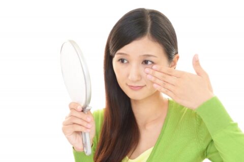 鏡で目の下 の 膨らみを見る女性