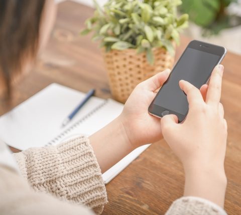 机に向かいスマホを操作する女性