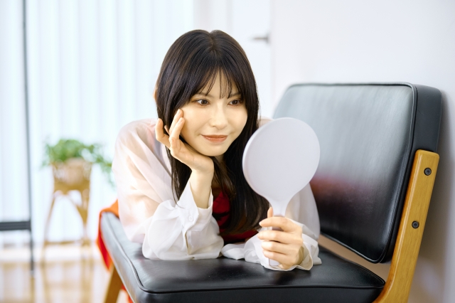 鏡を見つめ目元に手を添える若い女性