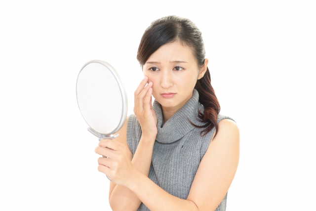不安そうに手鏡で目元を見つめる女性