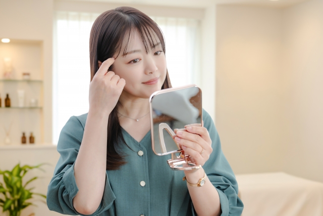 手に持った鏡を見ながら目元を指さす女性