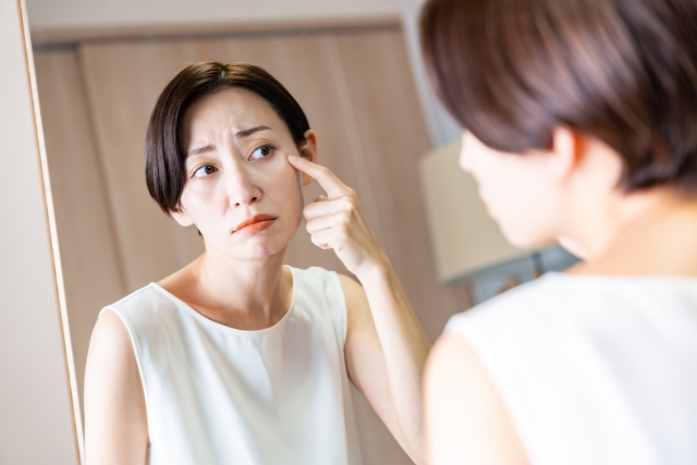 目の下を押さえて不安そうに鏡を見る女性