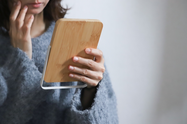薄暗い部屋で頬に手を添えながら鏡を見る女性