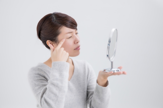 鏡を手に持ち目元を気にする女性