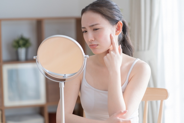 鏡を見ながら、左頬に手を当て、不満げな表情をする女性