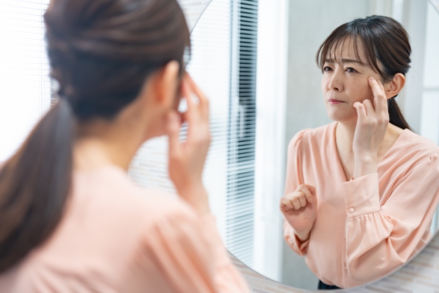 鏡を見て目元に手を当てる悩んだ表情の女性